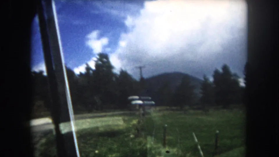 8mm home movie landscape from a moving vehicle showing Rocky Mountain scenery, cumulus clouds over a forested ridgeline, and a bus on the highway below, Summit County, Colorado, c. 1962.