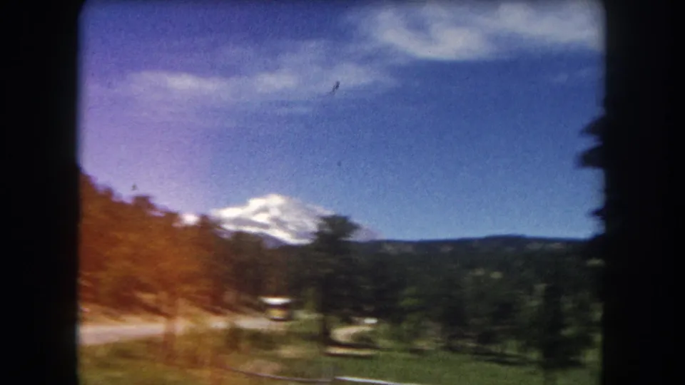 Final 1962 8mm frame from Summit County sequence showing strong motion blur, an orange color shift in the sky, a snow-capped peak, and a road with distant vehicles.