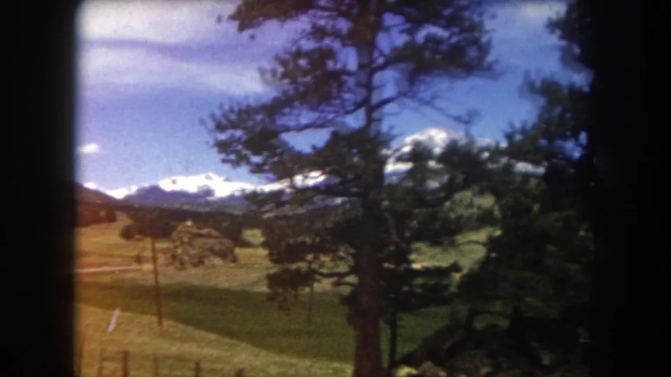 8mm home movie frame c. 1962 showing snow-capped mountains through pine trees with a roadside utility pole, Summit County, Colorado area.