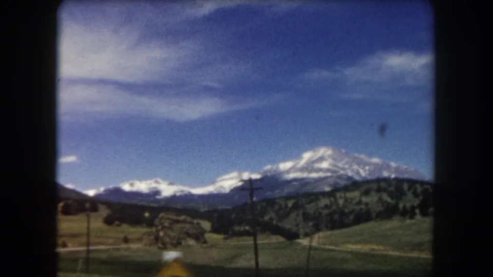 8mm home movie frame from 1962 showing a sweeping view of snow-capped peaks in the Summit County, Colorado area, with rocky terrain and power lines.