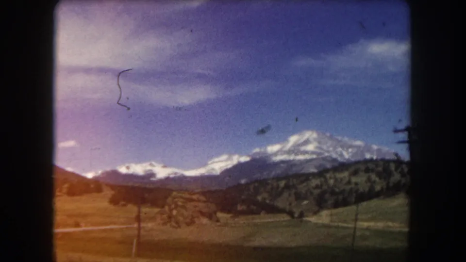 8mm home movie frame from c. 1962 showing snow-capped mountains in what appears to be Summit County, Colorado, with significant dye-layer fading producing a violet sky.