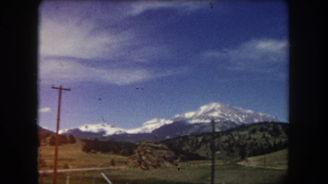 Snow-capped mountain with wooden telephone poles and rolling hills in foreground, 8mm color film.