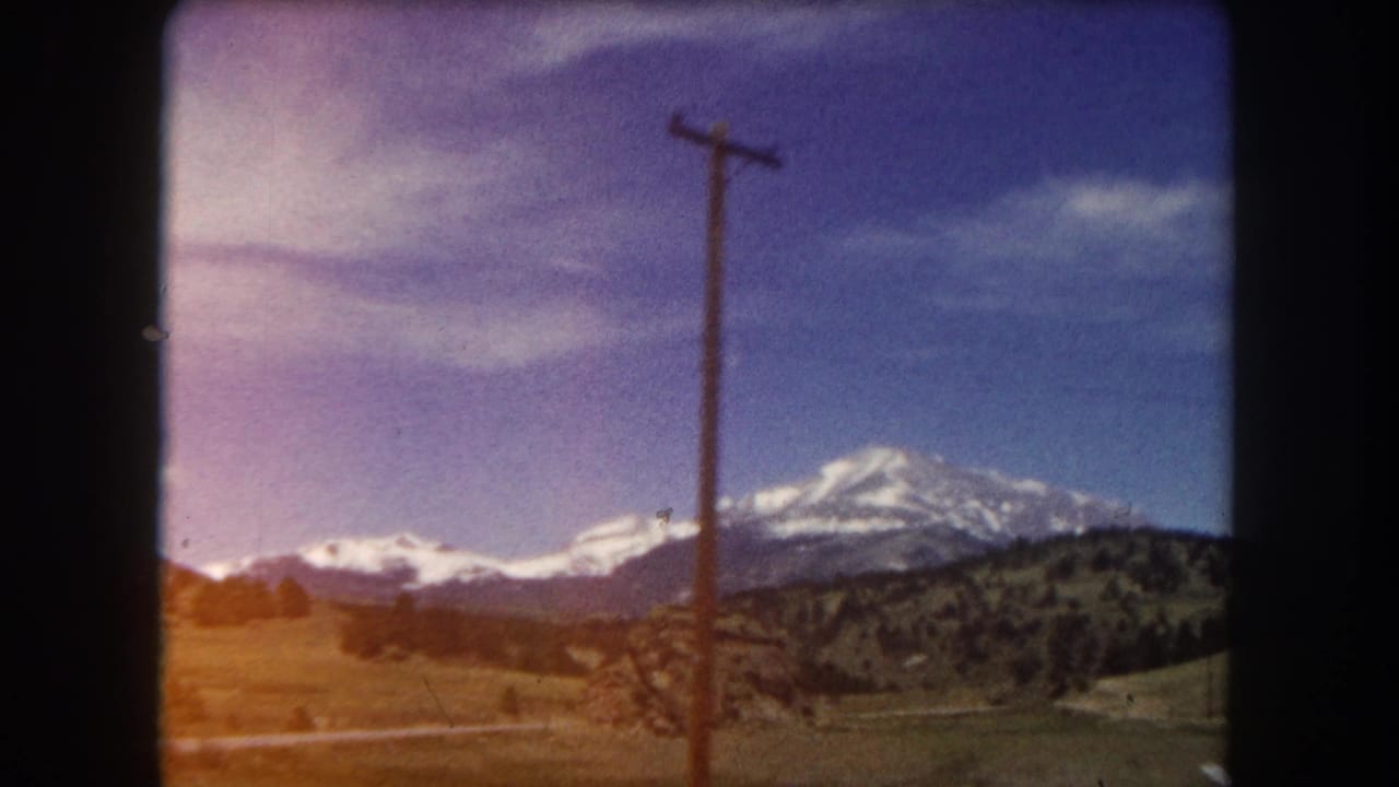 Mid-pan 8mm frame from Summit County, Colorado, 1962; snow-covered mountain and telephone pole under a sky with a visible magenta emulsion color shift.