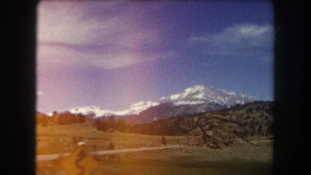 Snow-capped mountain peak above an open meadow with a curving dirt road, filmed on 8mm color stock.