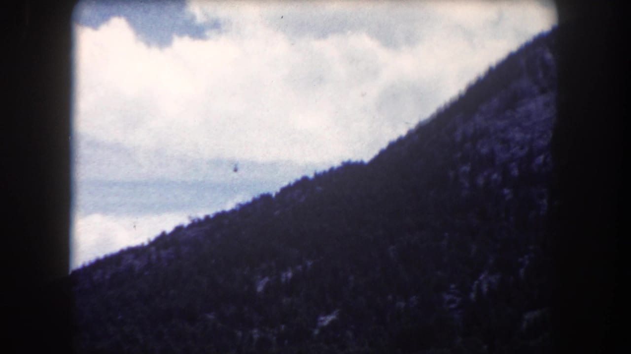 Forested mountain ridge rising diagonally against a partly cloudy sky, shot on 8mm with heavy corner vignetting.