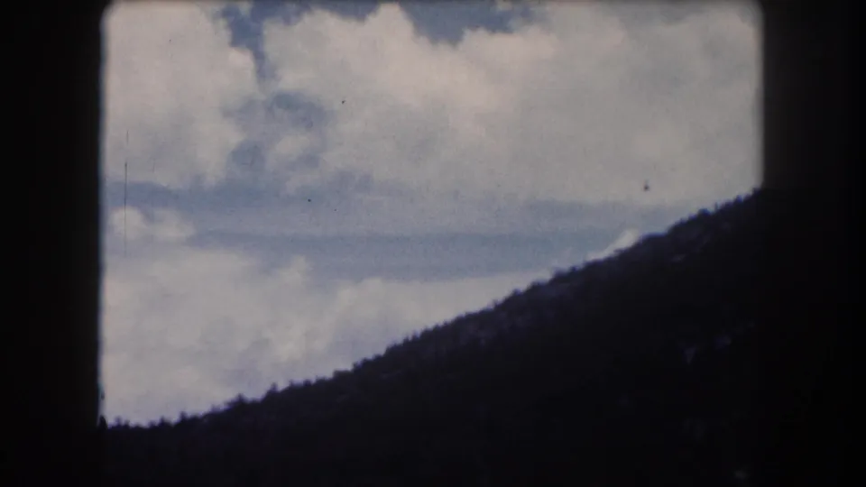 8mm footage circa 1962, final pan frame showing broad cumulus cloud formations over a low forested ridgeline, Summit County, Colorado.