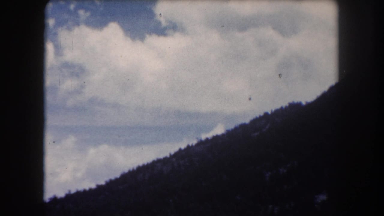 8mm home-movie frame circa 1962, Summit County Colorado: billowing cumulus clouds rising above a dark forested ridge as blue sky recedes