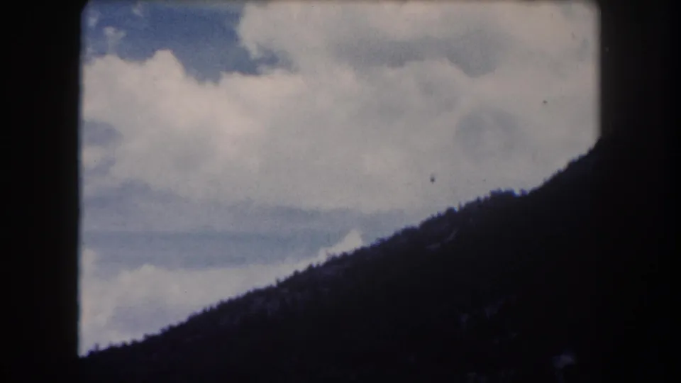 8mm home-movie frame circa 1962, Summit County Colorado: large cumulus cloud mass filling most of the sky above a dark forested ridge
