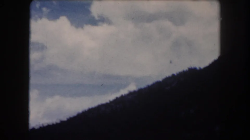 8mm home-movie frame circa 1962, Summit County Colorado: dense billowing cumulus clouds above a forested ridge with little blue sky remaining