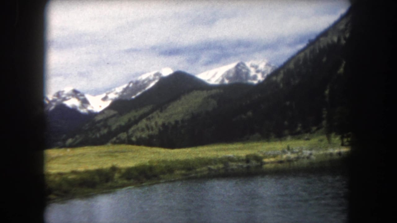 8mm film frame of snow-capped Rocky Mountain peaks above an open alpine meadow with conifer slopes, Summit County, Colorado, circa 1962.