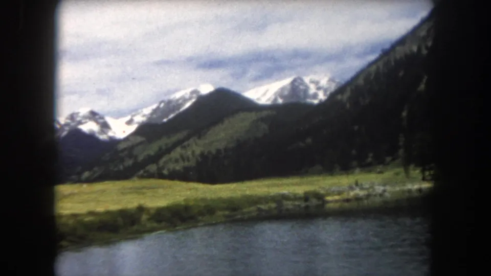 8mm film frame of snow-capped Rocky Mountain peaks above an open alpine meadow with conifer slopes, Summit County, Colorado, circa 1962.