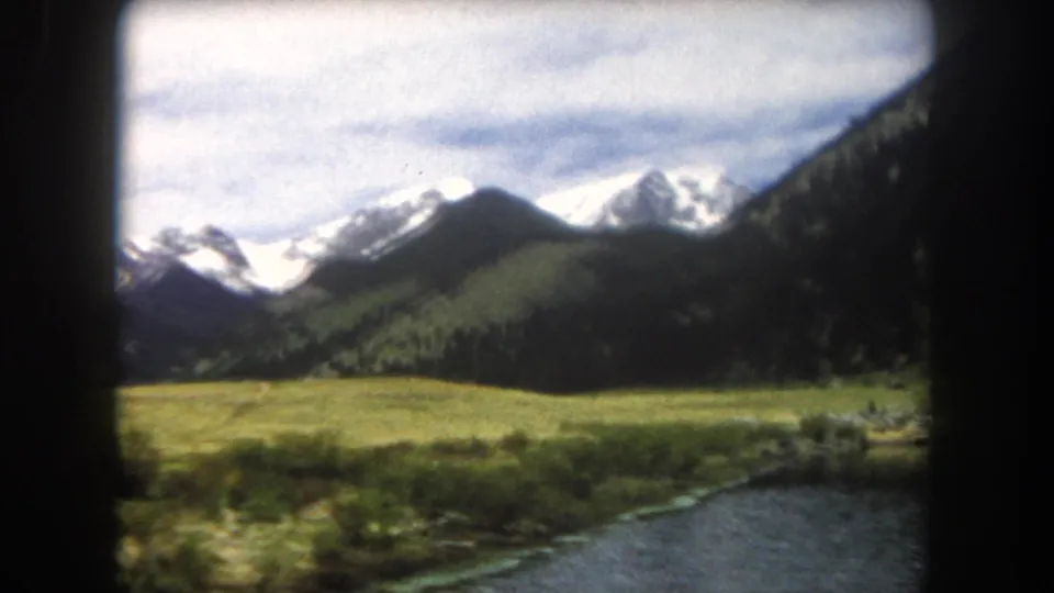 8mm film frame showing a mountain stream and low riparian shrubs in the foreground with snow-capped peaks beyond, Summit County, Colorado, circa 1962.