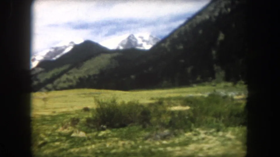 8mm film frame of an open alpine meadow with low shrubby foreground vegetation and snow-capped Rocky Mountain peaks, Summit County, Colorado, circa 1962.