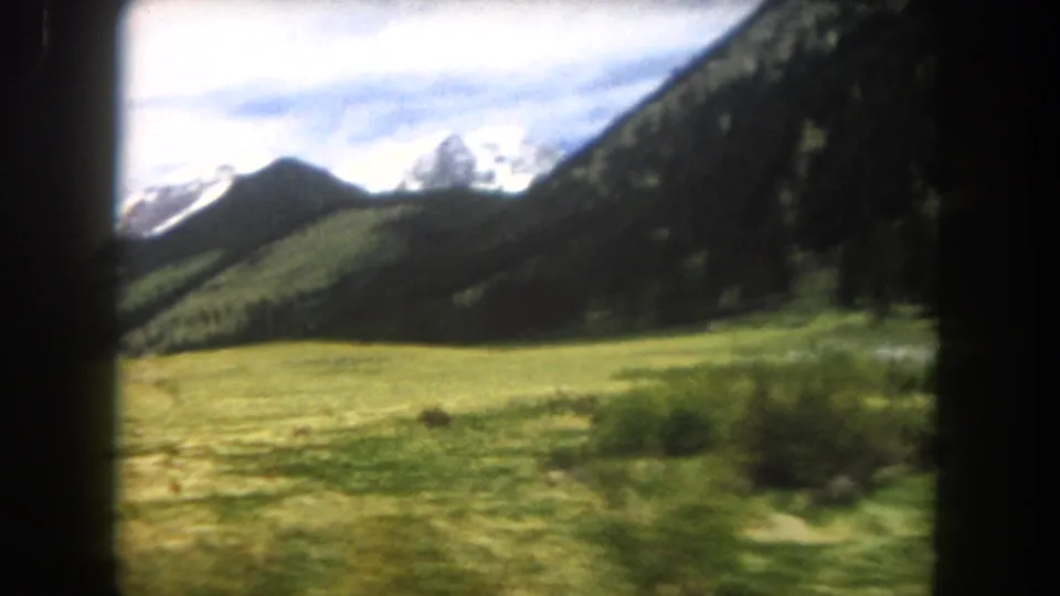 8mm home-movie frame, circa 1962, of an open mountain meadow and snow-capped Rocky Mountain peaks in Summit County, Colorado, viewed from a moving car.