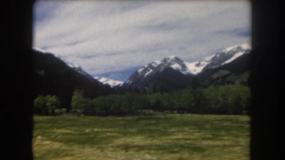 8mm color film, ca. 1962, Summit County, Colorado; the panning motion reveals a broader Rocky Mountain panorama of snow-capped peaks above the open alpine valley floor.