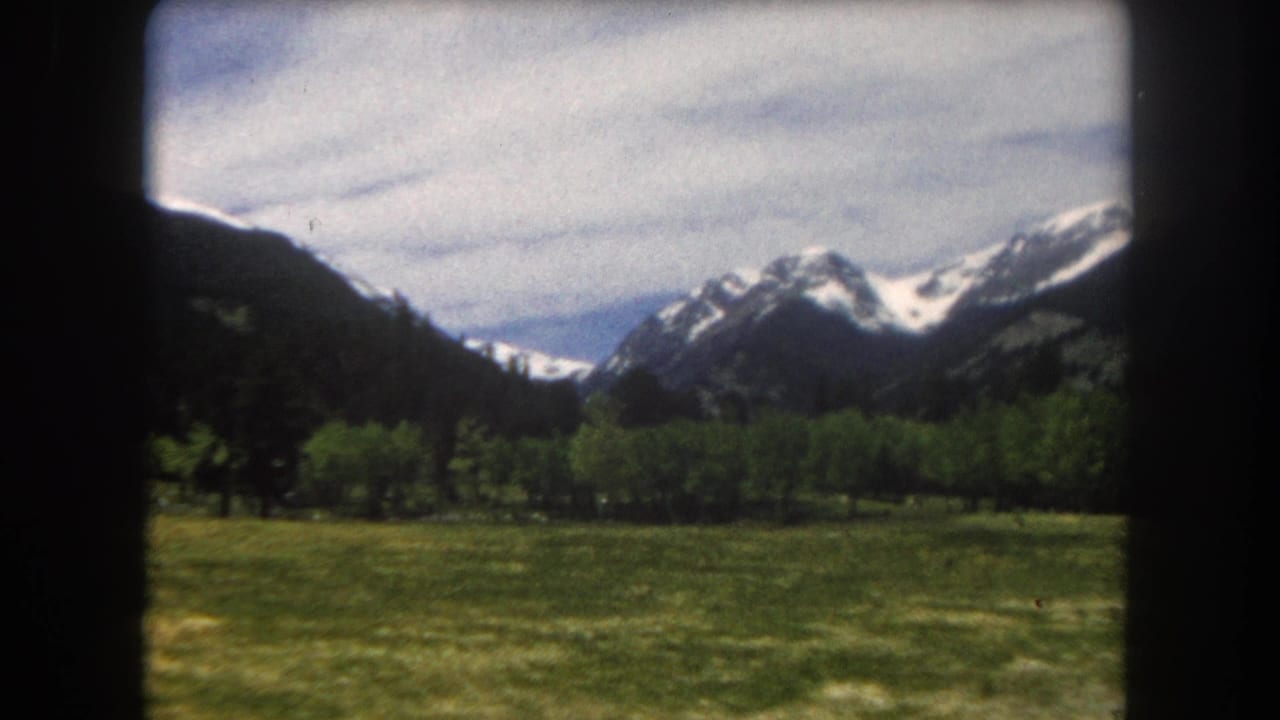 Mountain panorama with green valley meadow and snow-capped peaks, 8mm film, slight pan right.