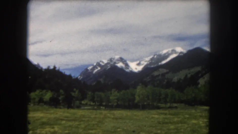 Final 8mm frame of Colorado Rocky Mountain valley — camera panned right to reveal additional snow-covered peaks and forested ridgeline, Summit County area.