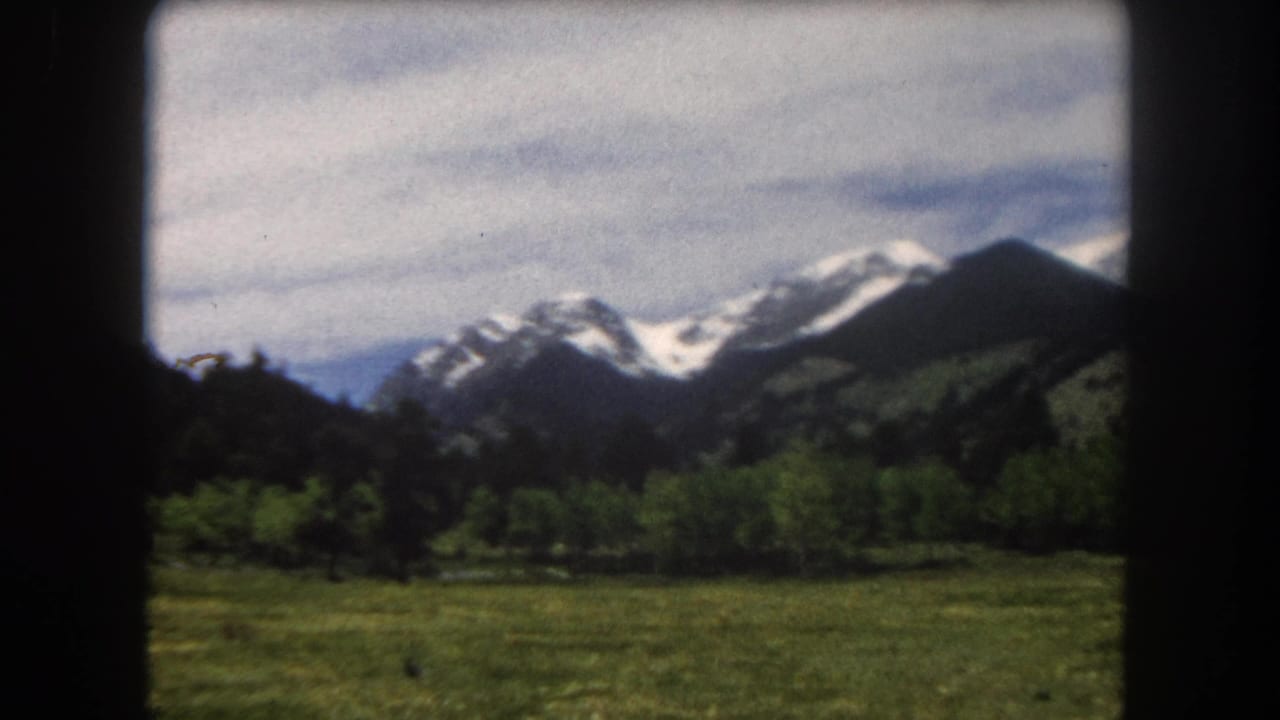 Snow-capped Rocky Mountain peaks rise above a green summer meadow, 8mm home movie, c. 1962.