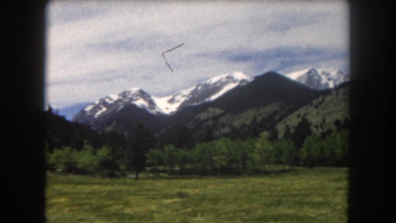 Continued pan across snow-covered Rocky Mountain peaks and green valley, slight camera shift, 8mm, c. 1962.