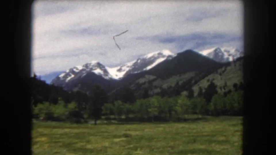Pan across snow-capped Summit County peaks above a green valley, with a small film artifact visible upper right, 8mm home movie, 1962.