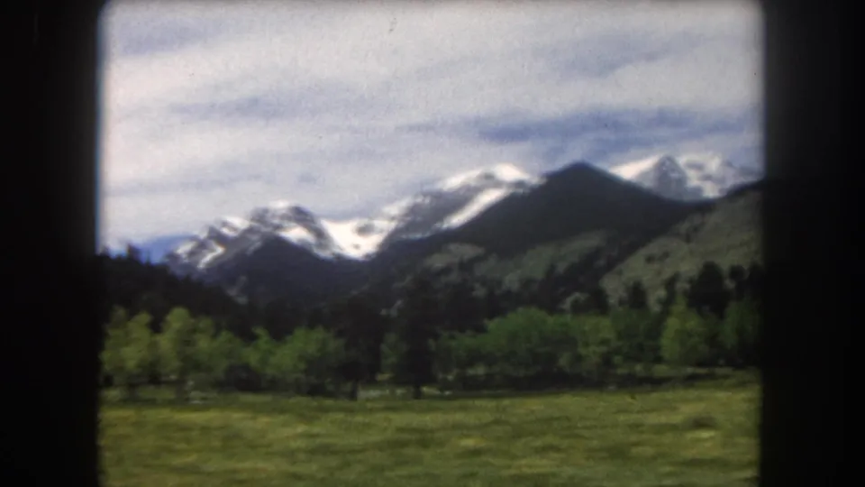 Shifted framing reveals Summit County snow-capped peaks rising above a green summer valley, 8mm home movie, 1962.