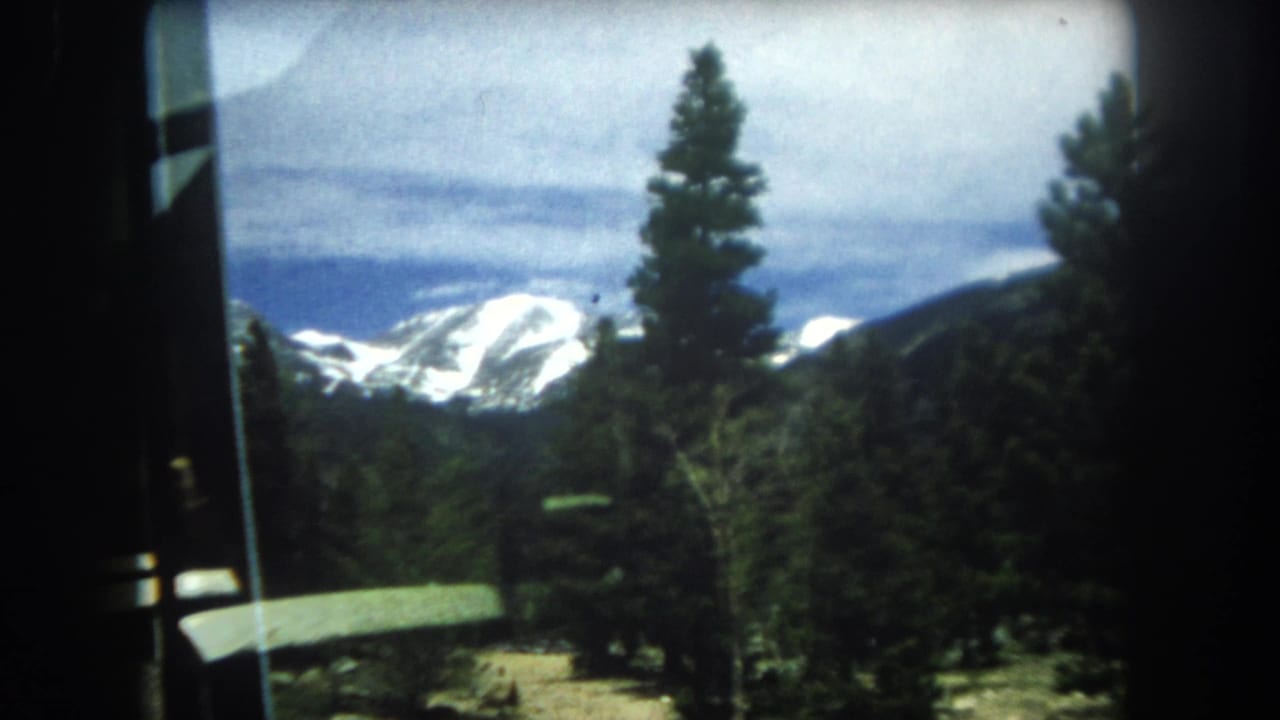 8mm home movie frame from 1962 showing snow-capped mountains in what metadata identifies as Summit County, Colorado, viewed through a window.