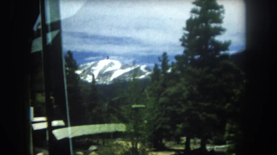8mm home movie frame circa 1962 showing snow-capped peaks in what appears to be Summit County, Colorado, shot through a vehicle or cabin window.
