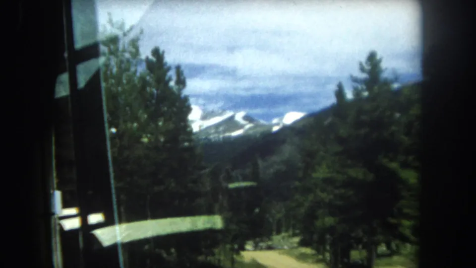 8mm frame circa 1962 showing a receding mountain vista through a window, with dense pine forest and cloudy sky, likely Summit County, Colorado.