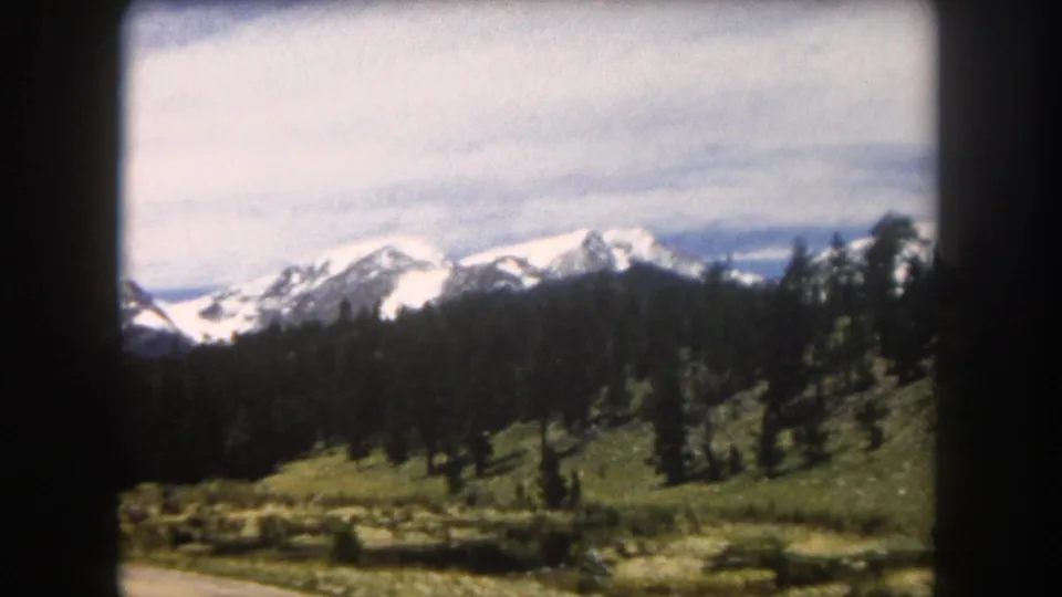 8mm color film, circa 1962: snow-covered peaks rise above conifer slopes and an alpine meadow, likely Summit County, Colorado.