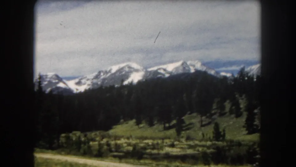 8mm color film, circa 1962: snow-capped peaks and pine slopes with a visible diagonal film scratch, likely Summit County, Colorado.
