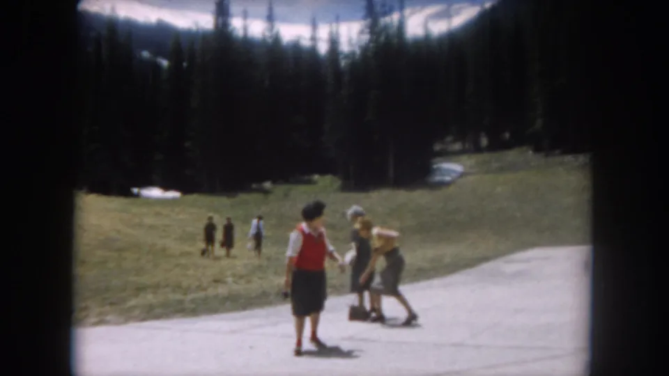 Woman in red top and dark skirt on a Colorado mountain path with additional figures, possibly including younger visitors, joining the scene; circa 1962.
