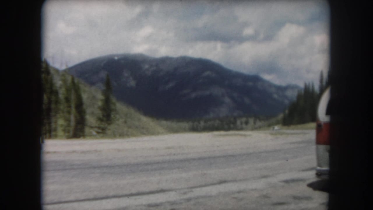 Continuation of 8mm driving sequence circa 1962 showing the same Summit County mountain road and red-and-white vehicle under partial cloud cover.