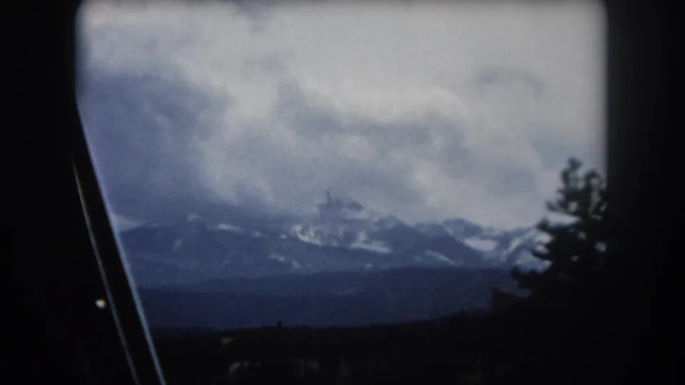 Through-windshield 8mm shot circa 1962 of Rocky Mountain slopes with conifer forest and distant peaks, Summit County, Colorado.