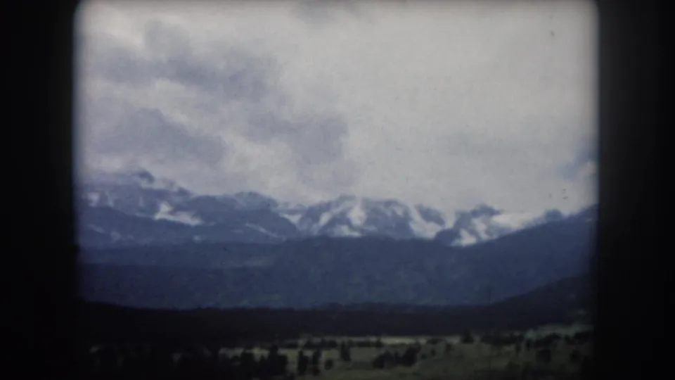 8mm pan frame showing a snow-capped mountain range under heavy cloud cover above a wide valley, Summit County, Colorado, circa 1962.