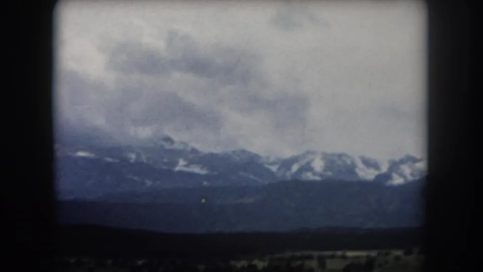 8mm home movie end-of-pan frame showing snow-capped peaks and wide valley floor under partly cloudy skies, Summit County, Colorado, circa 1962.