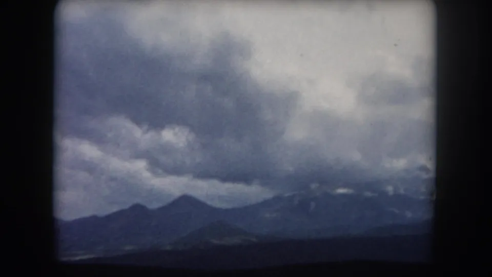 1962 Summit County, Colorado 8mm frame with dark mountain silhouettes beneath layered storm clouds.