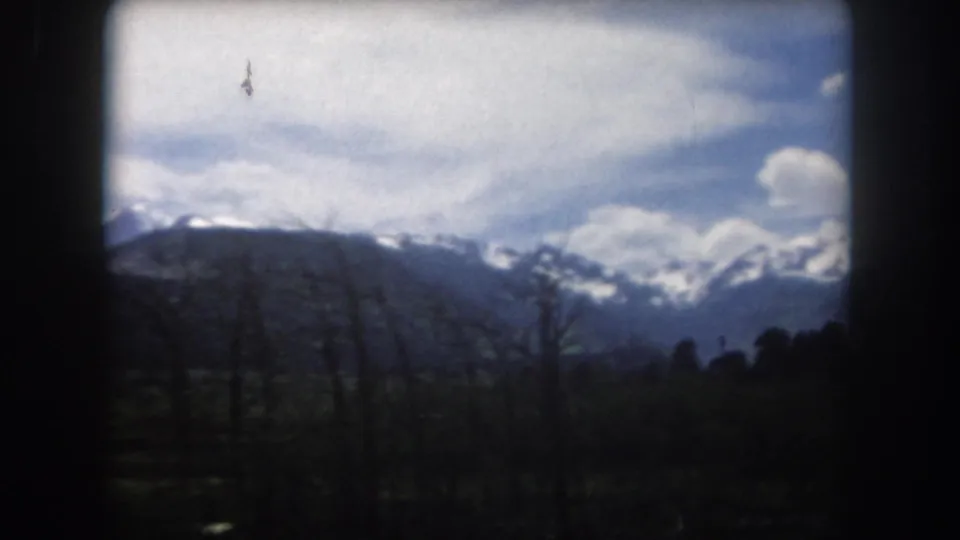1962 Summit County, Colorado 8mm frame with snow-bright mountain peaks beyond dark trees and a shaded valley foreground.