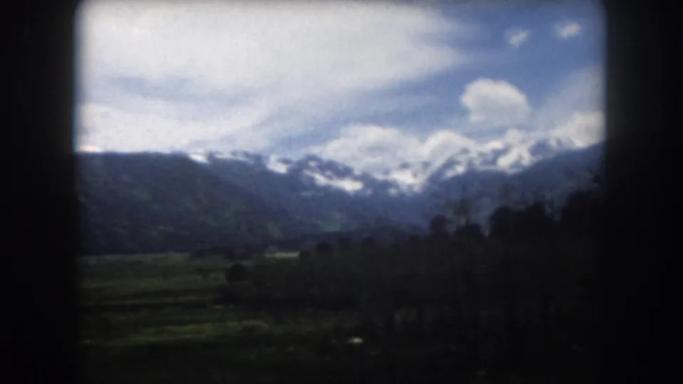 1962 Summit County, Colorado mountain view with snow-streaked peaks, green valley patches, and dark foreground trees.
