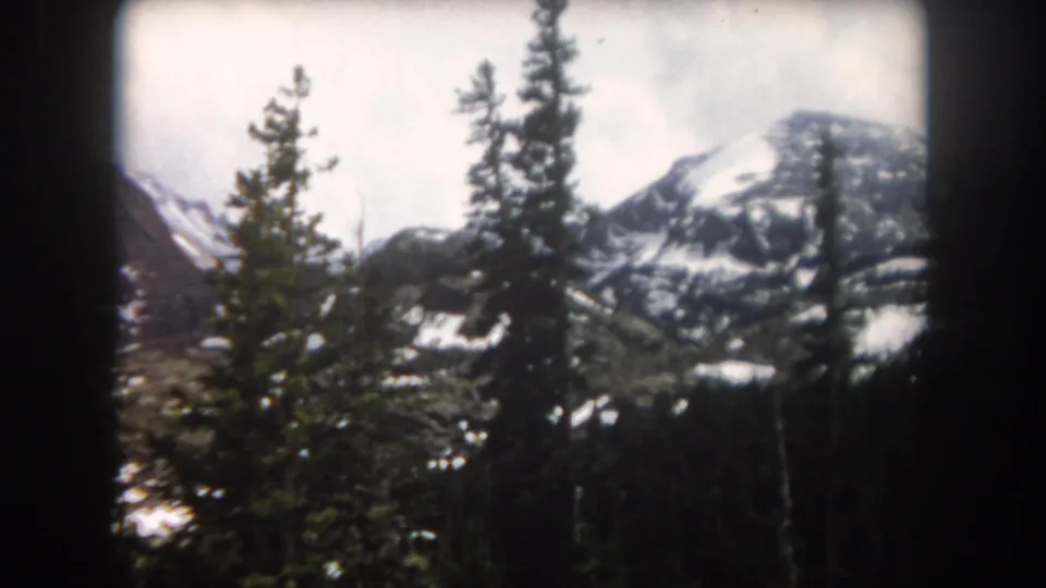 1962 Summit County, Colorado frame showing evergreen trees in the foreground with snow-streaked alpine slopes behind them.