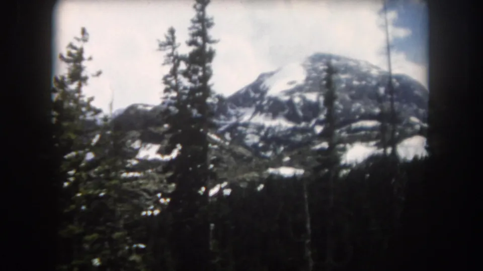 1962 Summit County, Colorado 8mm shot with tall pines in front of a rounded, snow-streaked mountain summit.