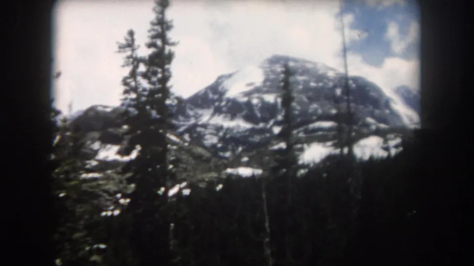 1962 Summit County, Colorado frame showing a snowy mountain face through evergreen trees, with soft focus and visible 8mm borders.