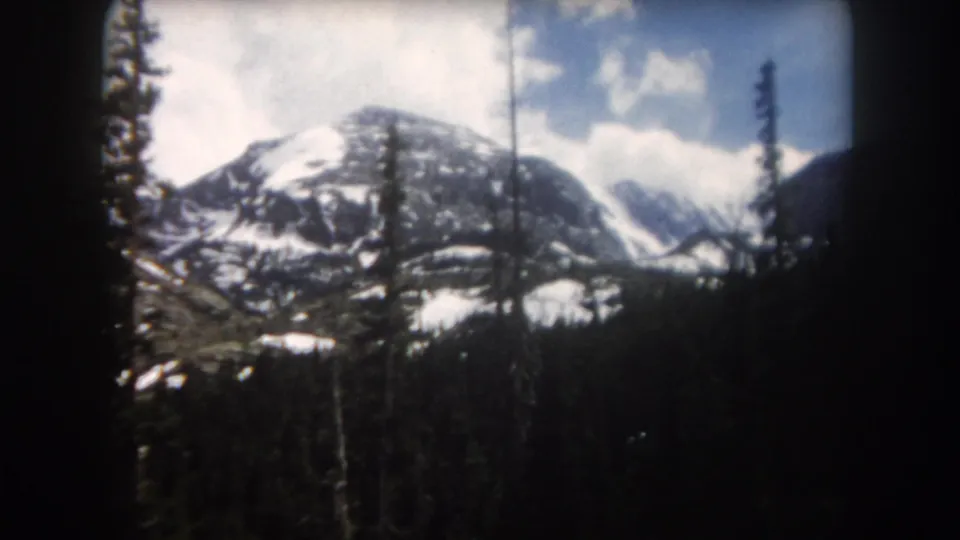 1962 Summit County, Colorado frame with a snow-covered mountain beyond evergreens, clouds, and dark rounded 8mm frame edges.