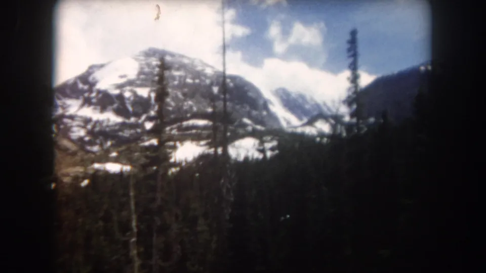 Summit County, Colorado mountain landscape on 8mm film, with snow patches, evergreen trees, and a partly cloudy sky.