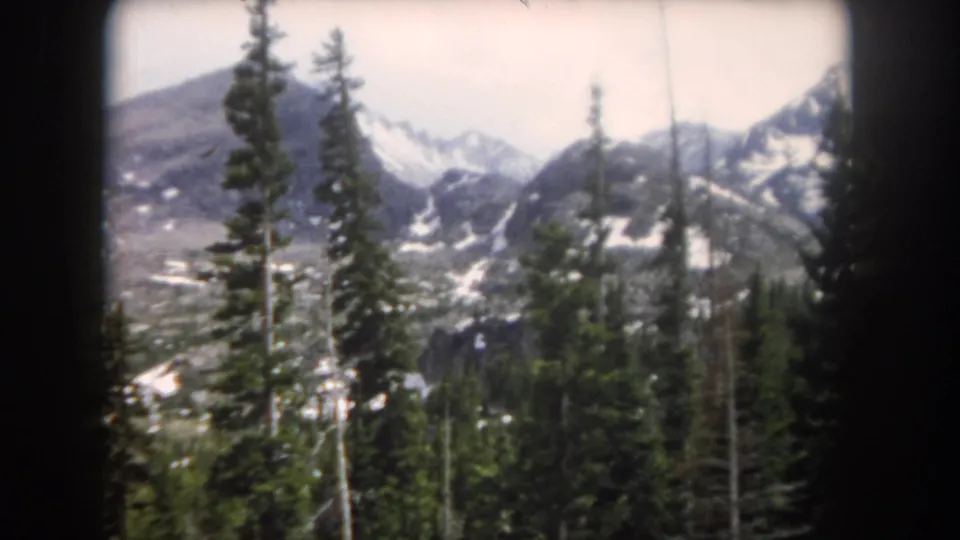 1962 Summit County, Colorado view of evergreen forest with distant snowy peaks and rugged alpine slopes in soft 8mm color.