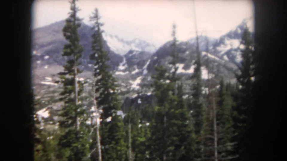 1962 Summit County, Colorado home-movie still of evergreens before dark alpine slopes and scattered snow in the Rockies.