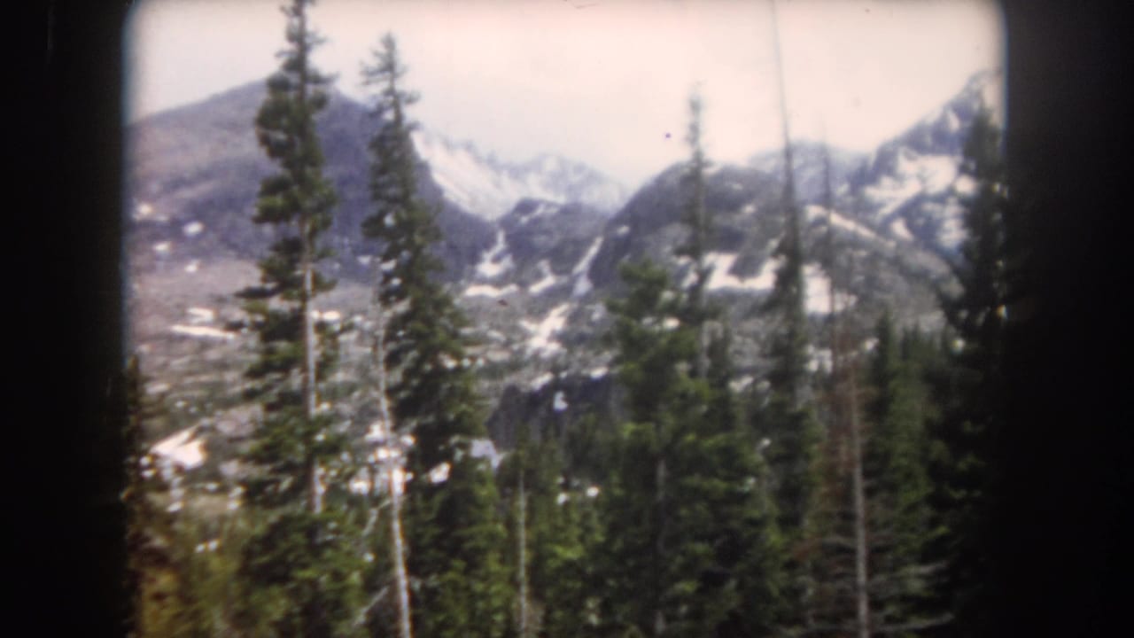 1962 Summit County, Colorado home-movie view of snow-dusted mountains with conifer trees in the foreground.