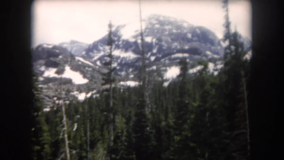 Vintage 8mm view of Summit County mountains, with dense pines in the foreground and lingering snow across rocky slopes.