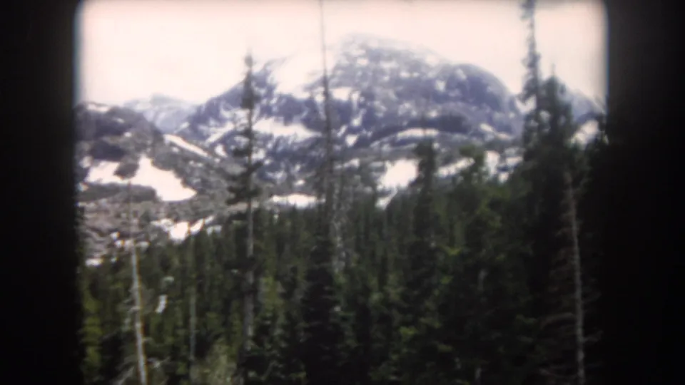 Summit County, Colorado landscape frame from 1962 showing pine forest beneath a snow-marked mountain ridge and pale sky.