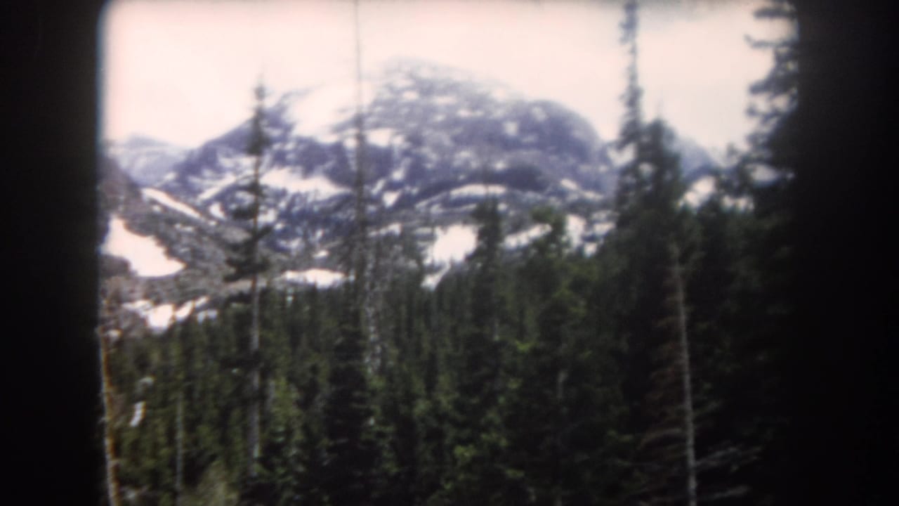 1962 Summit County, Colorado 8mm frame showing snow-patched mountains behind a pine forest, partly framed by dark film edges.