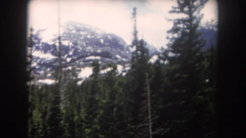 Summit County, Colorado mountain view on 8mm film, with pine trees in the foreground and lingering snow on the distant ridge.